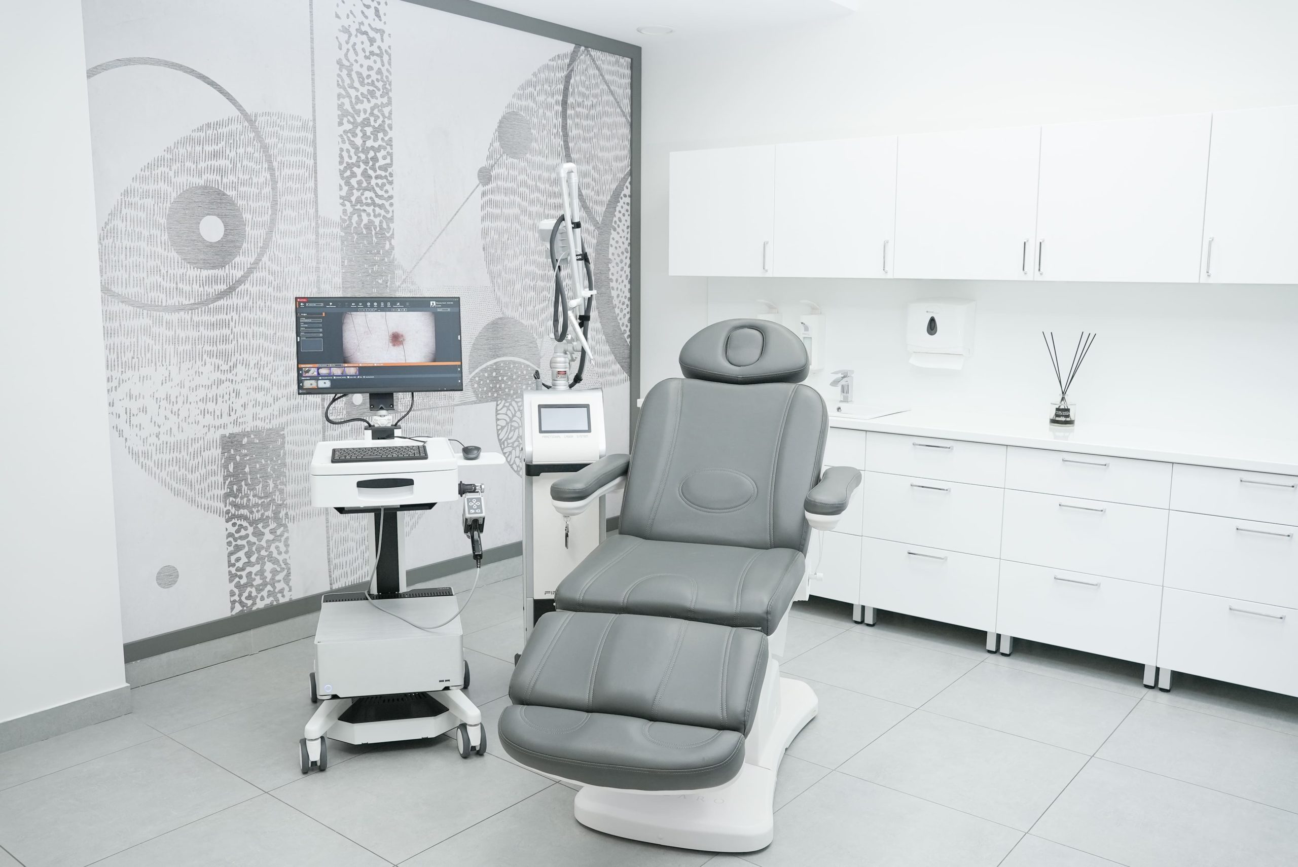 Gabinet dermatologiczny w Centrum Dermatologicznym FEBUMED w Warszawie przy ul. Popularnej 13 z wideodermatoskopem FotoFinder Vexia i laserem frakcyjnym obok fotela.
