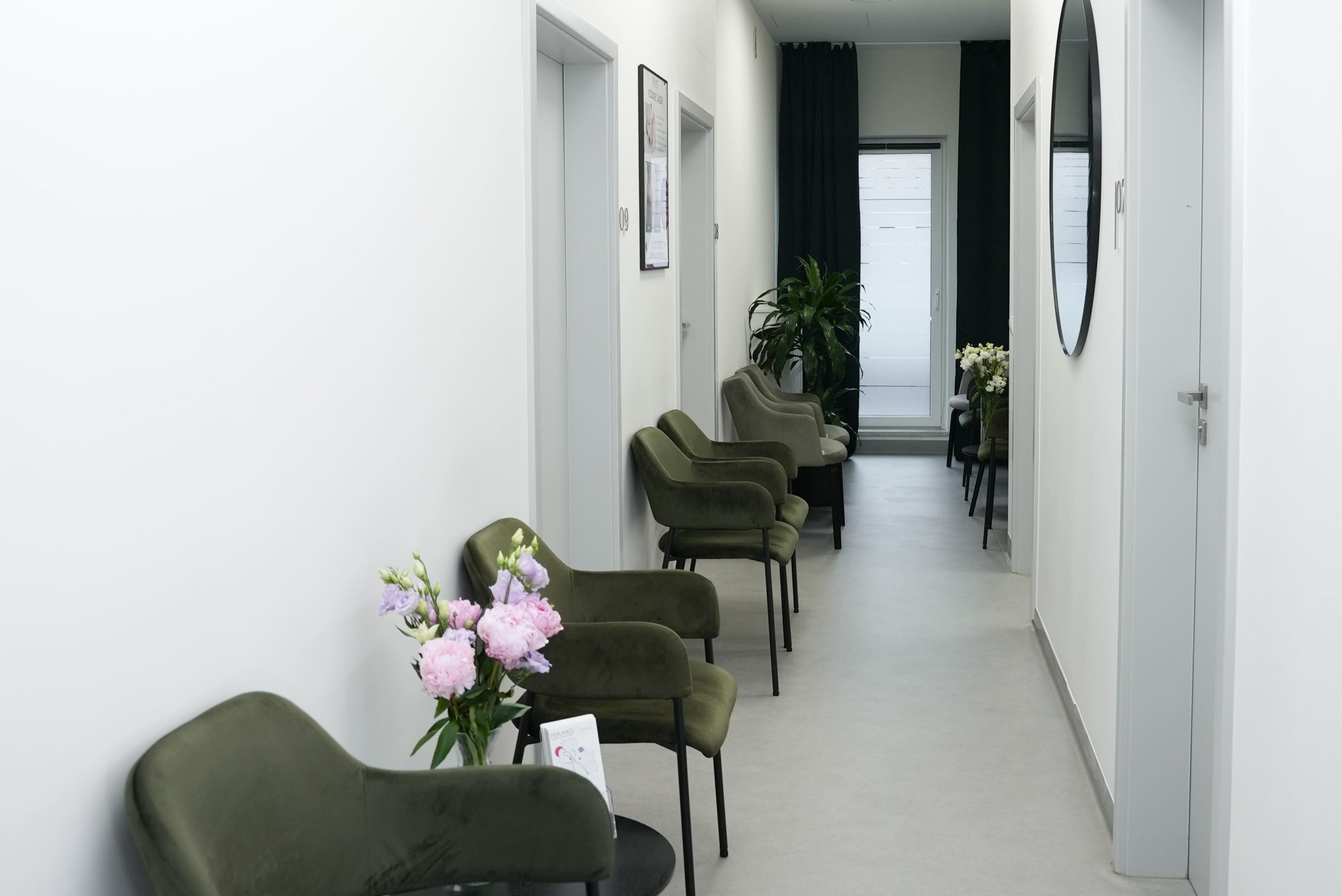 Elegancka poczekalnia na piętrze w Centrum Dermatologicznym FEBUMED w Warszawie przy ul. Popularnej 13 z zielonymi krzesłami i różowymi kwiatami.