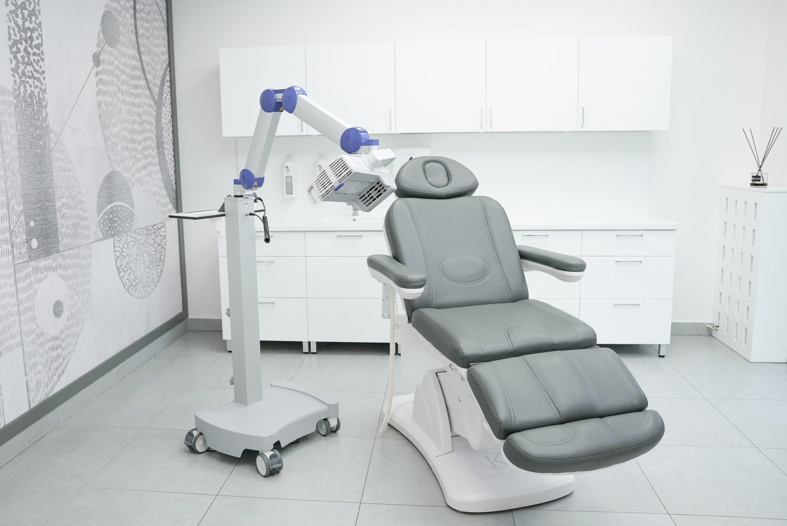 Gabinet lekarski w FEBUMED przy ul. Popularnej 13 w Warszawie - fotel medyczny, szara tapeta, białe meble i urządzenie do fototerapii PDT.