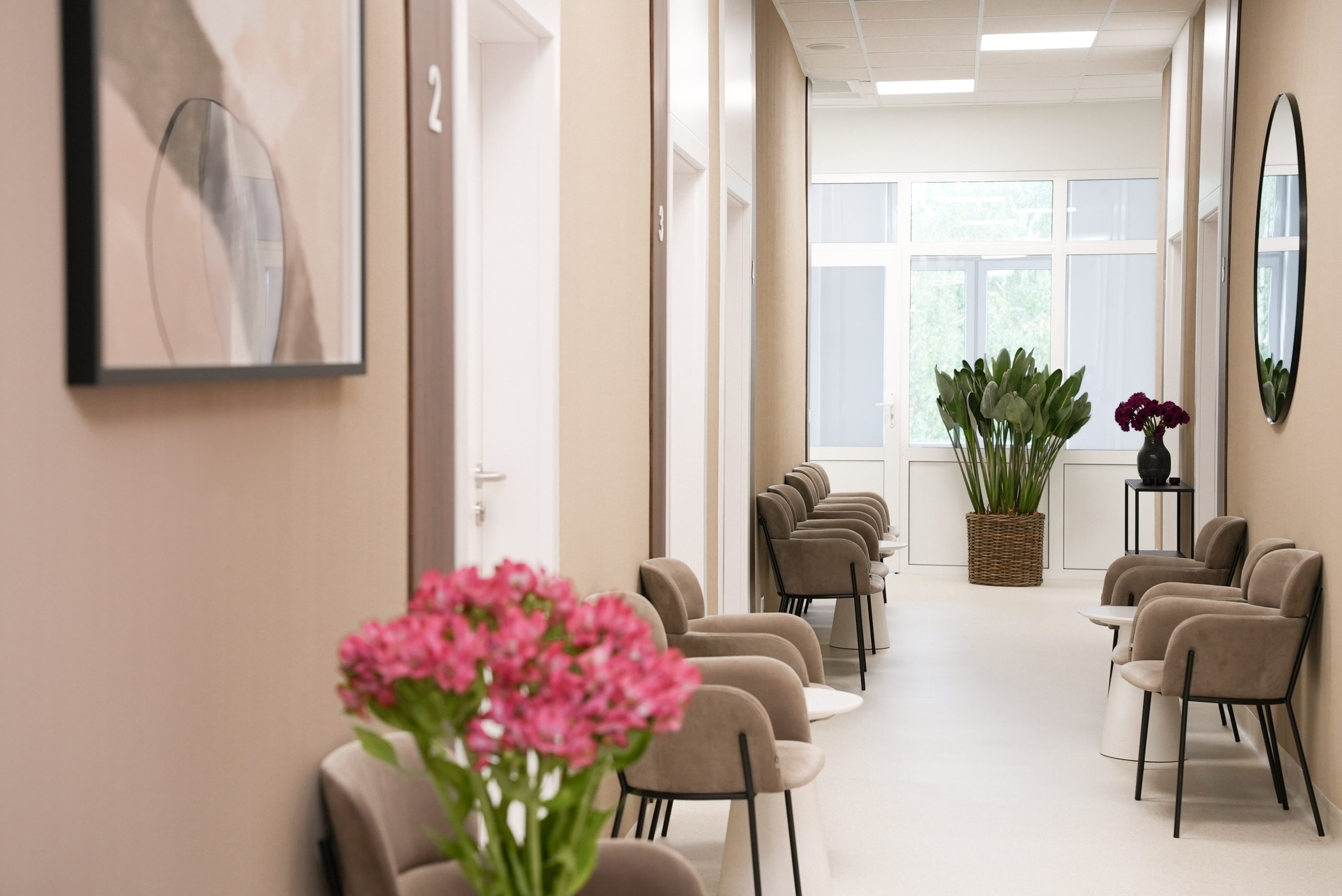 Poczekalnia w FEBUMED Praga Południe - stylowe brązowe wnętrza, miękkie krzesła, lustro, obrazy i kwiaty w doniczkach.