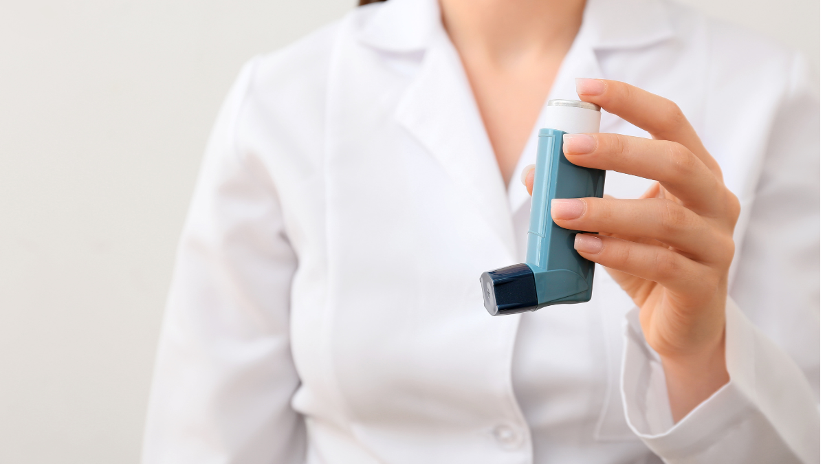 Lekarka w fartuchu trzymająca w lewej ręce mały przenośny niebieski inhalator