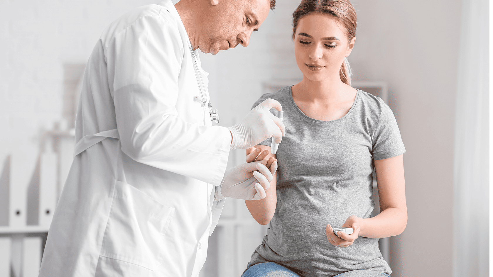 Lekarz diabetolog w białym fartuchu wykonujący badanie poziomu cukru we krwi, siedzącej młodej kobiecie w szarej bluzce za pomocą glukometru.
