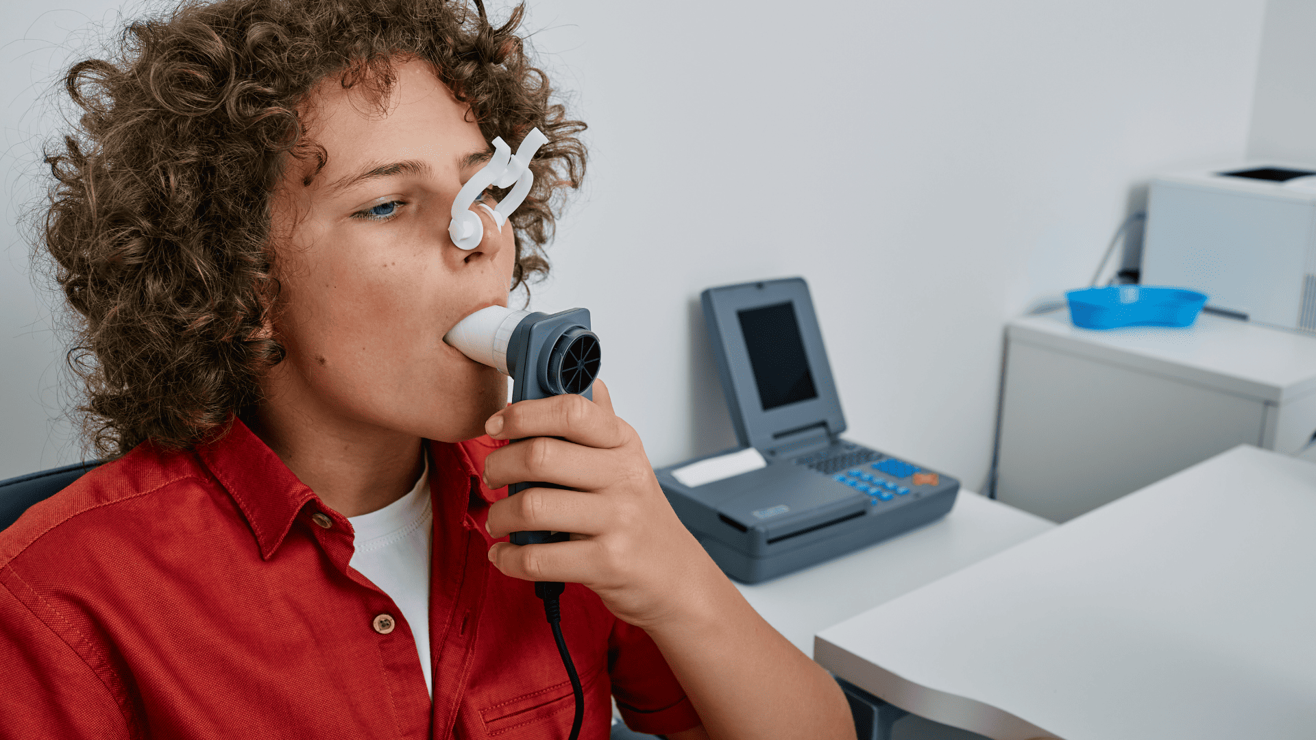 pacjent, który trzyma ustnik w buzi oraz ma medyczny klips na nosie podczas wykonywania badania spirometrycznego