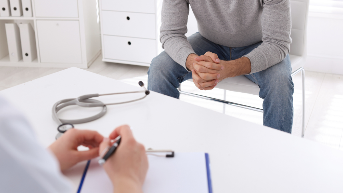 Lekarz omawiający i zapisujący problemy z pacjentem siedzącym na przeciwko niego na krześle.