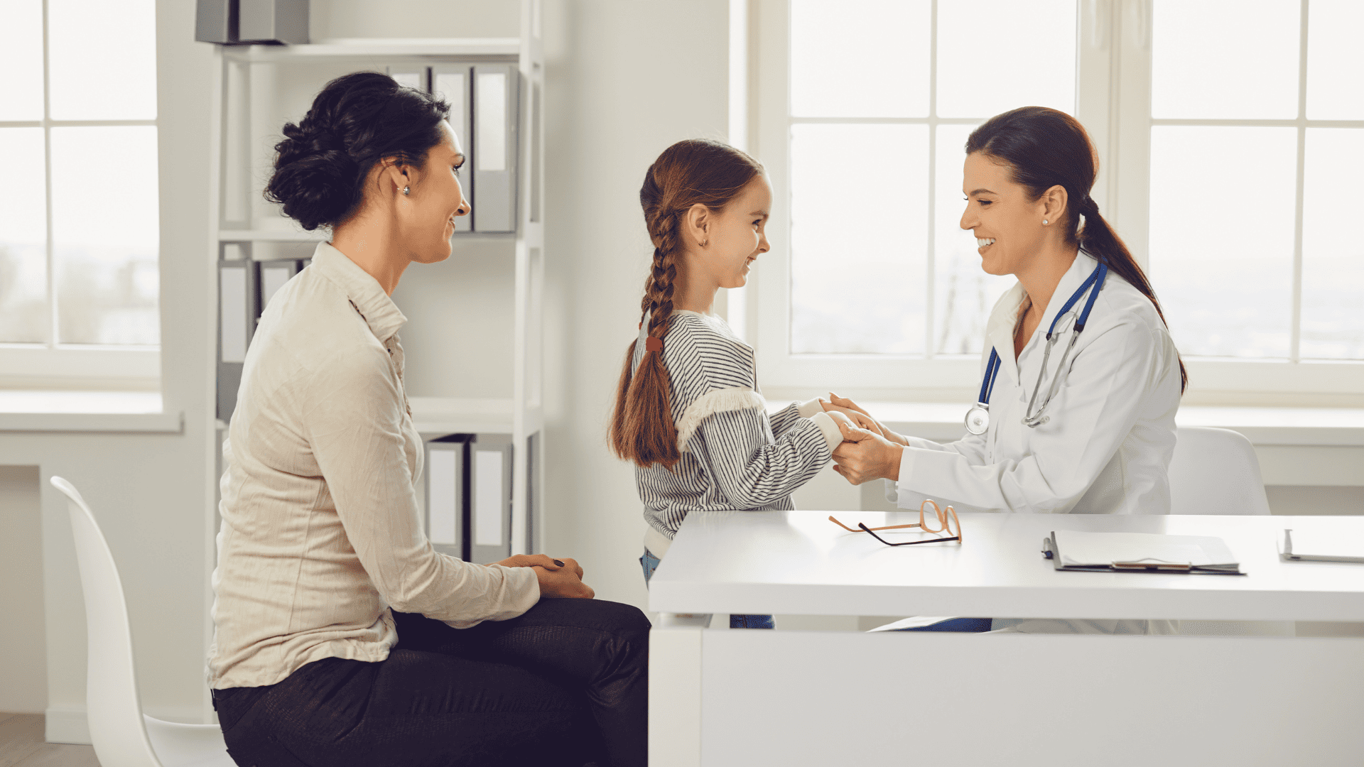 Lekarka ogląda rączki dziewczynki w gabinecie, dziewczynka jest uśmiechnięta obok siedzi jej mama.