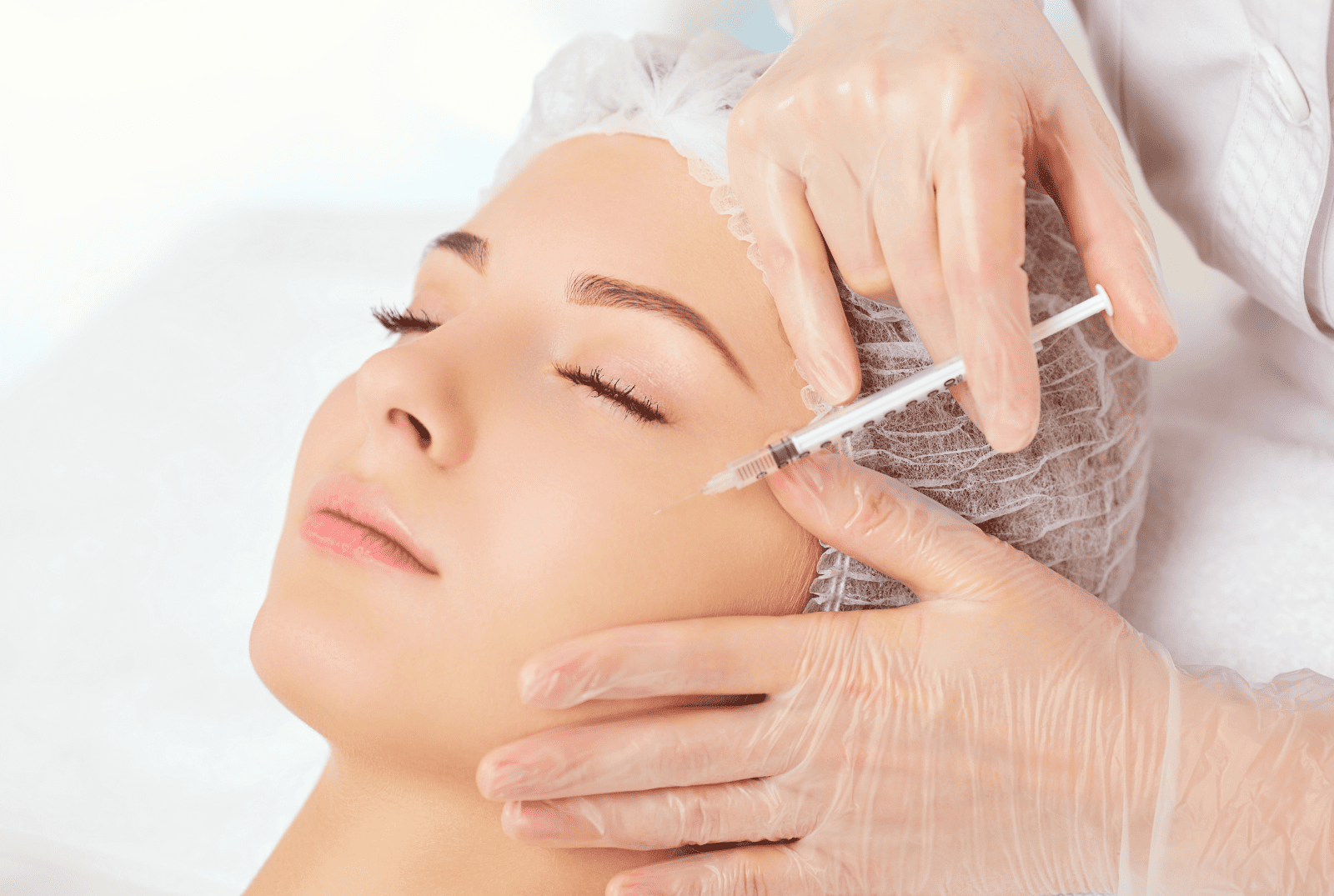 Zbliżenie na twarz młodej kobiety podczas gdy specjalista w rękawiczkach wykonuje na jej twarzy zabieg mezoterapii poprzez precyzyjne wprowadzenie substancji odżywczych wgłąb skóry za pomocą strzykawki