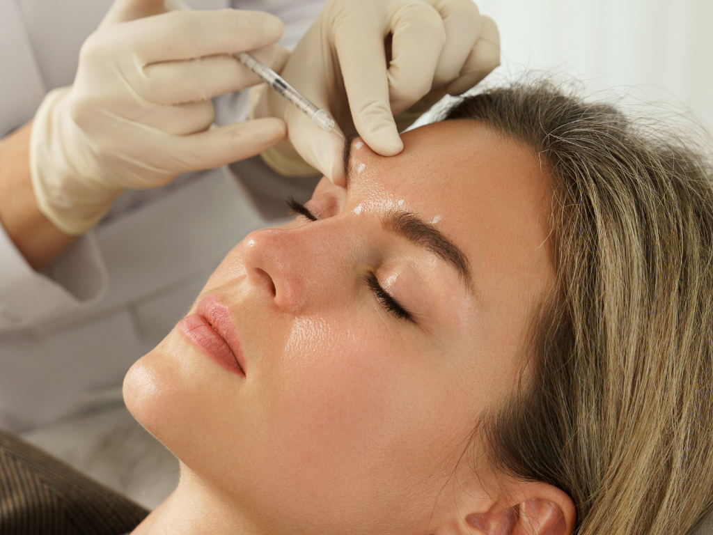 Pacjentka podczas zabiegu medycyny estetycznej – lekarz wykonuje iniekcję preparatu w okolice czoła