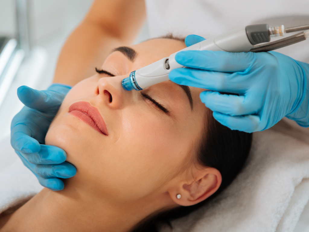 Kosmetolog w niebieskich rękawiczkach trzyma urządzenie do oczyszczania wodorowego podczas zabiegu u pacjentki