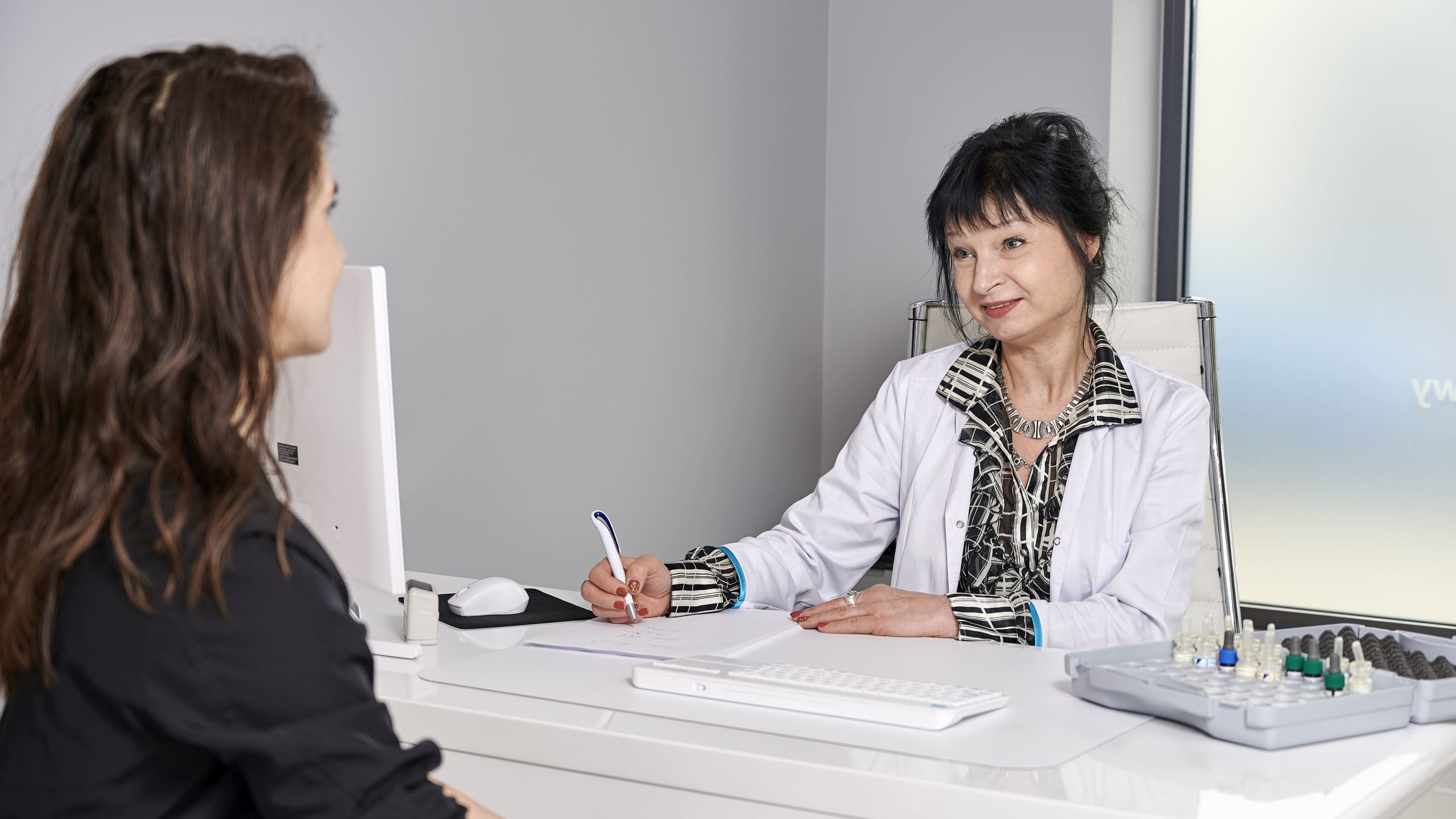 dr n. med. Beata Adamczyk podczas konsultacji alergologicznej z pacjentką, na biurku stoją fiolki z alergenami