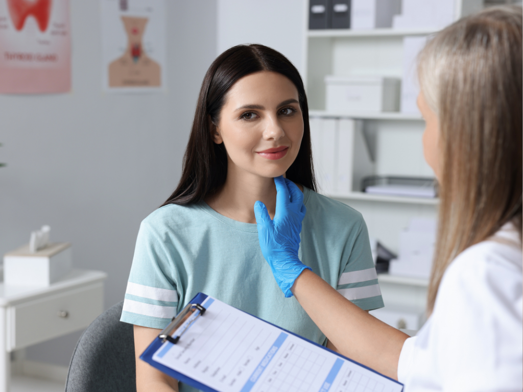 Endokrynolożka uciska szyję pacjentki podczas wstępnego badania palpacyjnego tarczycy w gabinecie