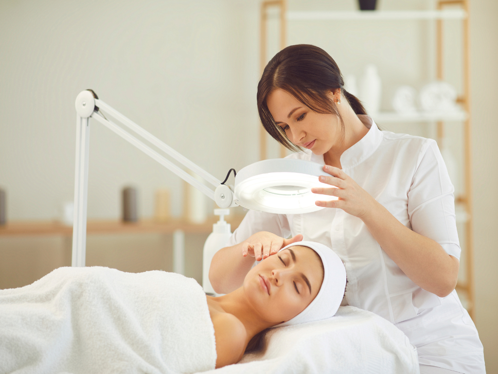 Kosmetolog ogląda twarz pacjentki pod lustrem powiększającym podczas konsultacji kosmetologicznej