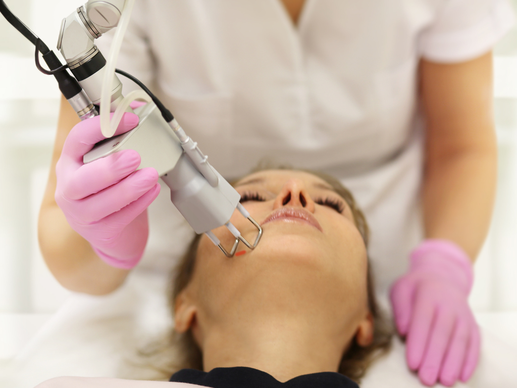 Lekarz przykłada urządzenie do twarzy pacjentki podczas zabiegu laserowego usuwania blizn