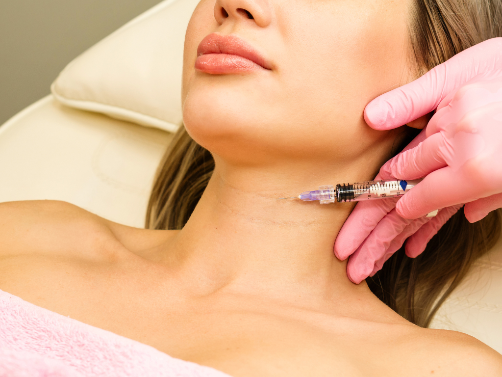 Lekarz w różowych rękawiczkach wykonuje zabieg biostymulacji mezoterapii na szyi pacjentki