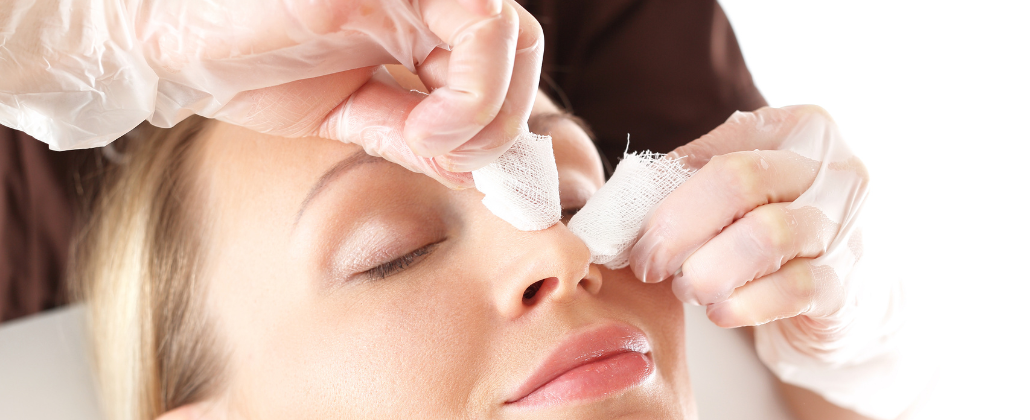 Kosmetolog przeprowadza oczyszczanie manualne twarzy pacjentki przy użyciu preparatów i gazików