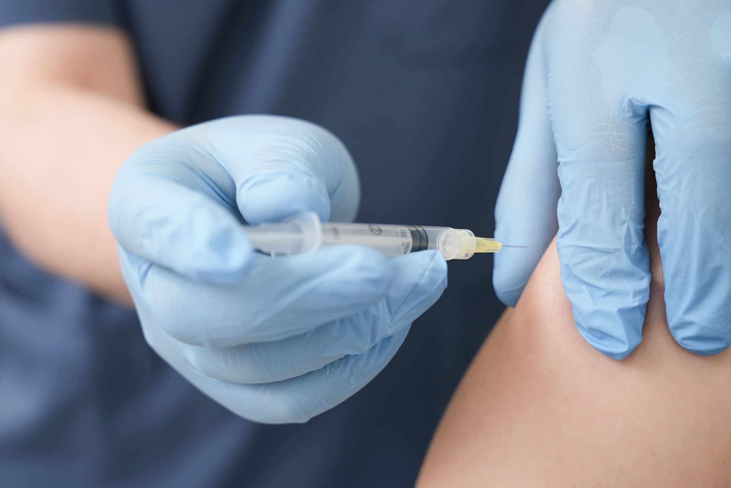 lekarz w rękawiczkach ze strzykawką w ręku tuż przed zaszczepieniem pacjentki w ramię