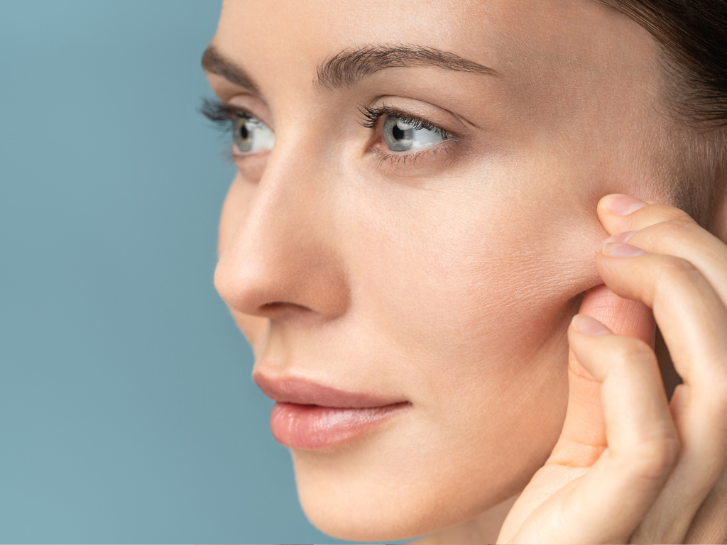 Pacjentka uciska lewy policzek, pokazując ubytek jędrności skóry przed zabiegiem biostymulacji